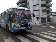 In Manta Equador setzt man auf bunte Busse.
Im Hintergrund ein vom Erdbeben beschädigtes Haus