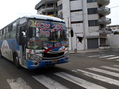 In Manta Equador setzt man auf bunte Busse. Im Hintergrund ein vom Erdbeben beschädigtes Haus